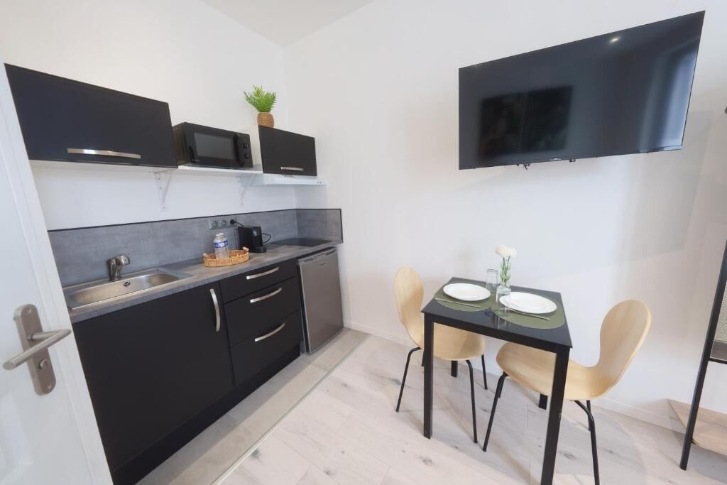 Eine kompakte Küche mit Mikrowelle, Spüle und Schränken, ein Esstisch mit Stühlen sowie ein flachbildfernseher an der Wand.