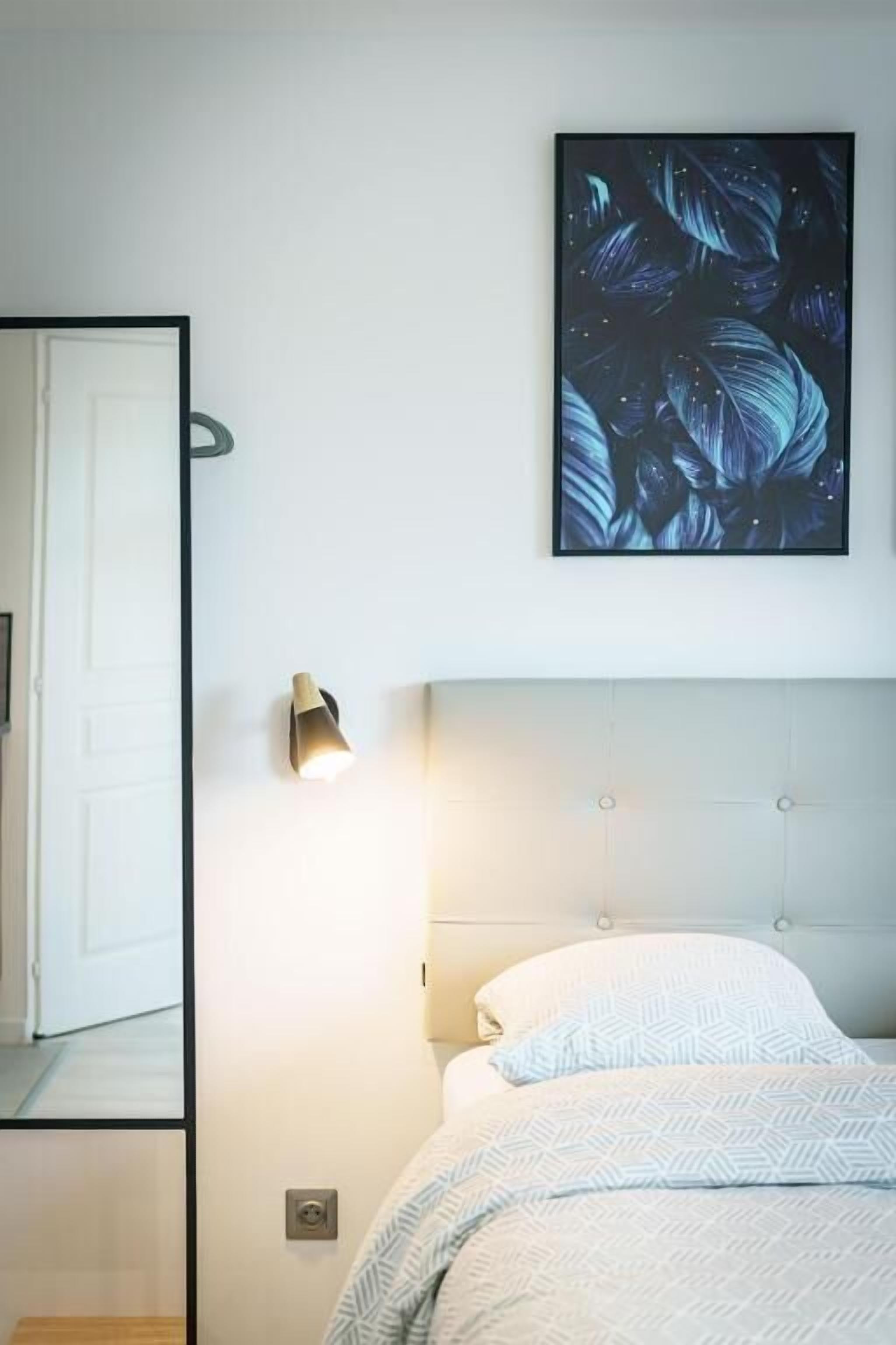 Un dormitorio con cama, luz empotrada en la pared y una obra de arte enmarcada sobre la cama.