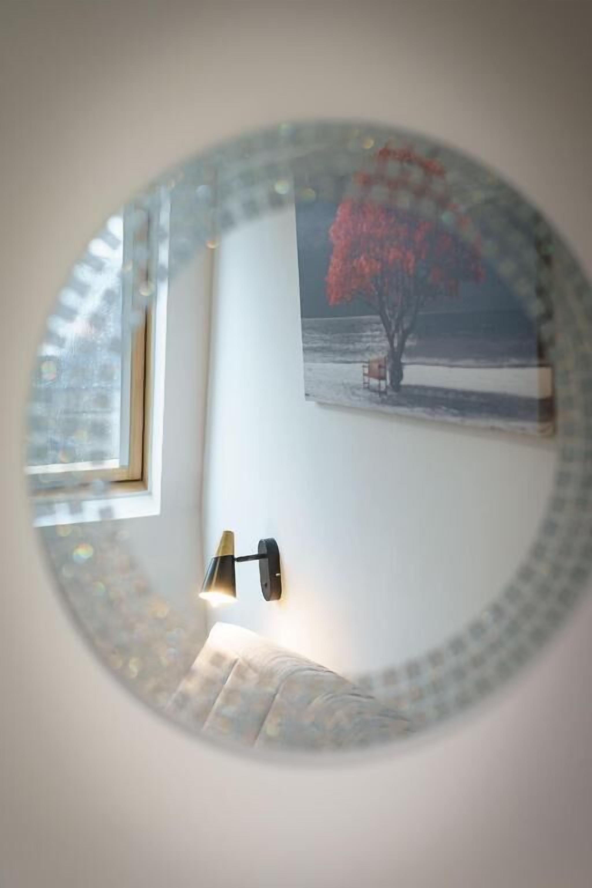 A round mirror with a reflection of a room, a window, and a lamp.