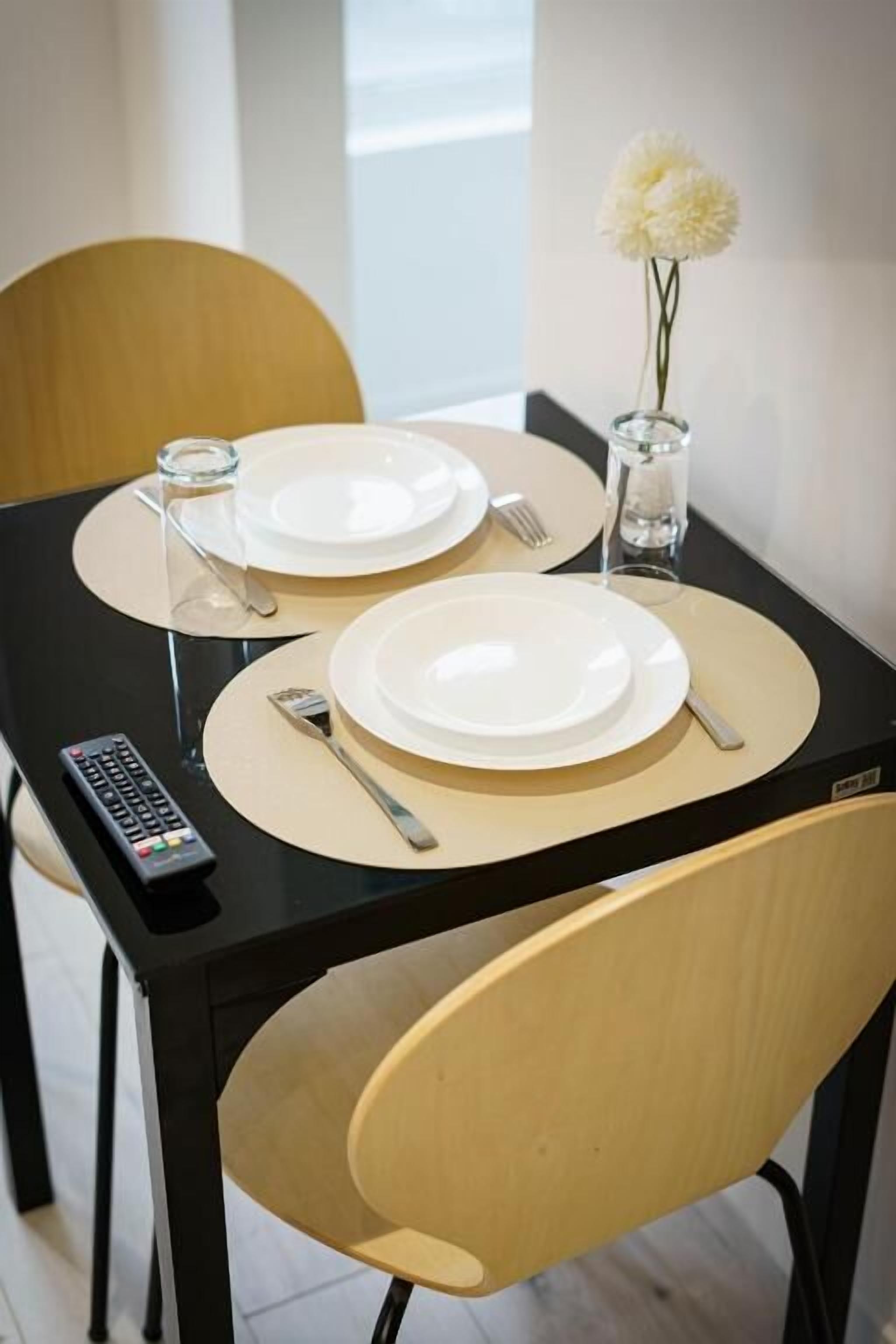 Uma mesa de jantar com dois pratos, talheres e um controle remoto.