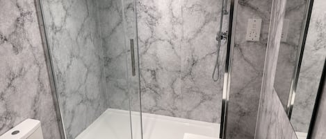 A modern bathroom with a glass-enclosed shower, a white toilet, and a sink with a chrome faucet.