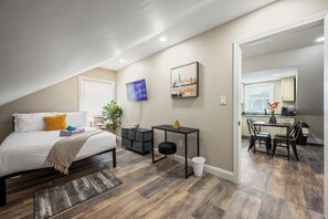 A bedroom with a bed, a desk, a chair, and a small table with a plant.