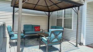 Een overdekt terras met een bank, stoelen en een tafel.