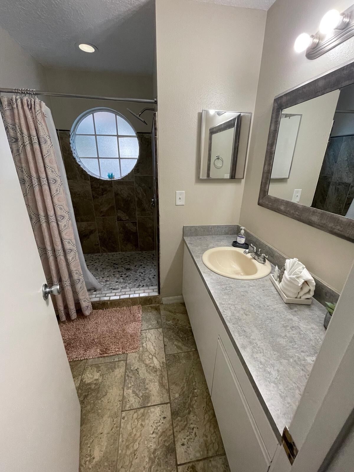 Une salle de bain avec une douche, un lavabo, un miroir et une fenêtre.
