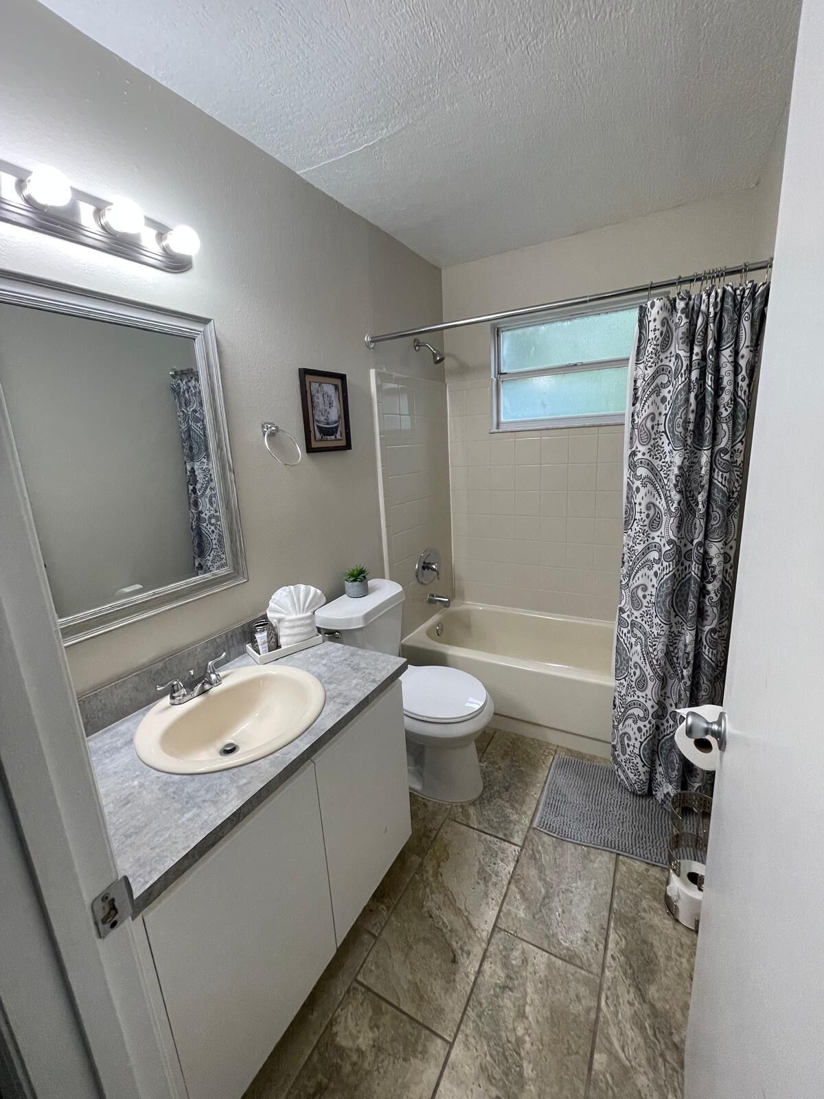 A bathroom with a sink, toilet, bathtub, shower curtain, and a window.