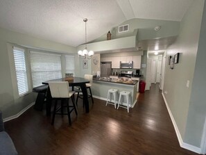A modern kitchen with a central island, dining area with chairs, and a hallway leading to a door. - A gateway close to Disney (Kissimmee)