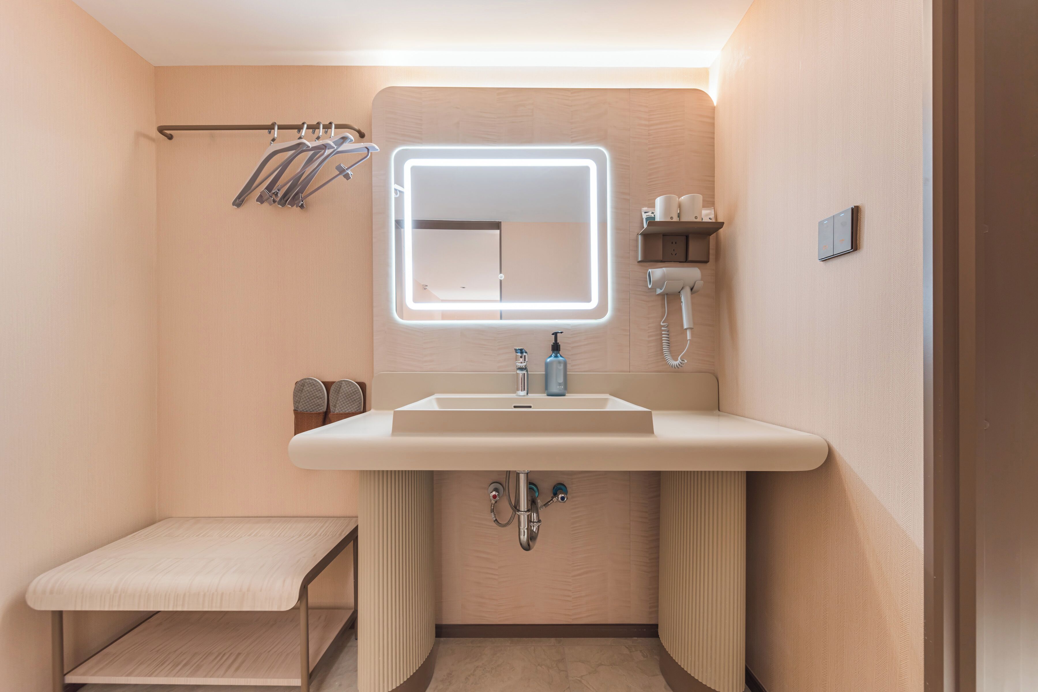 Un baño moderno con tocador, espejo con luces LED, perchero y un pequeño banco.