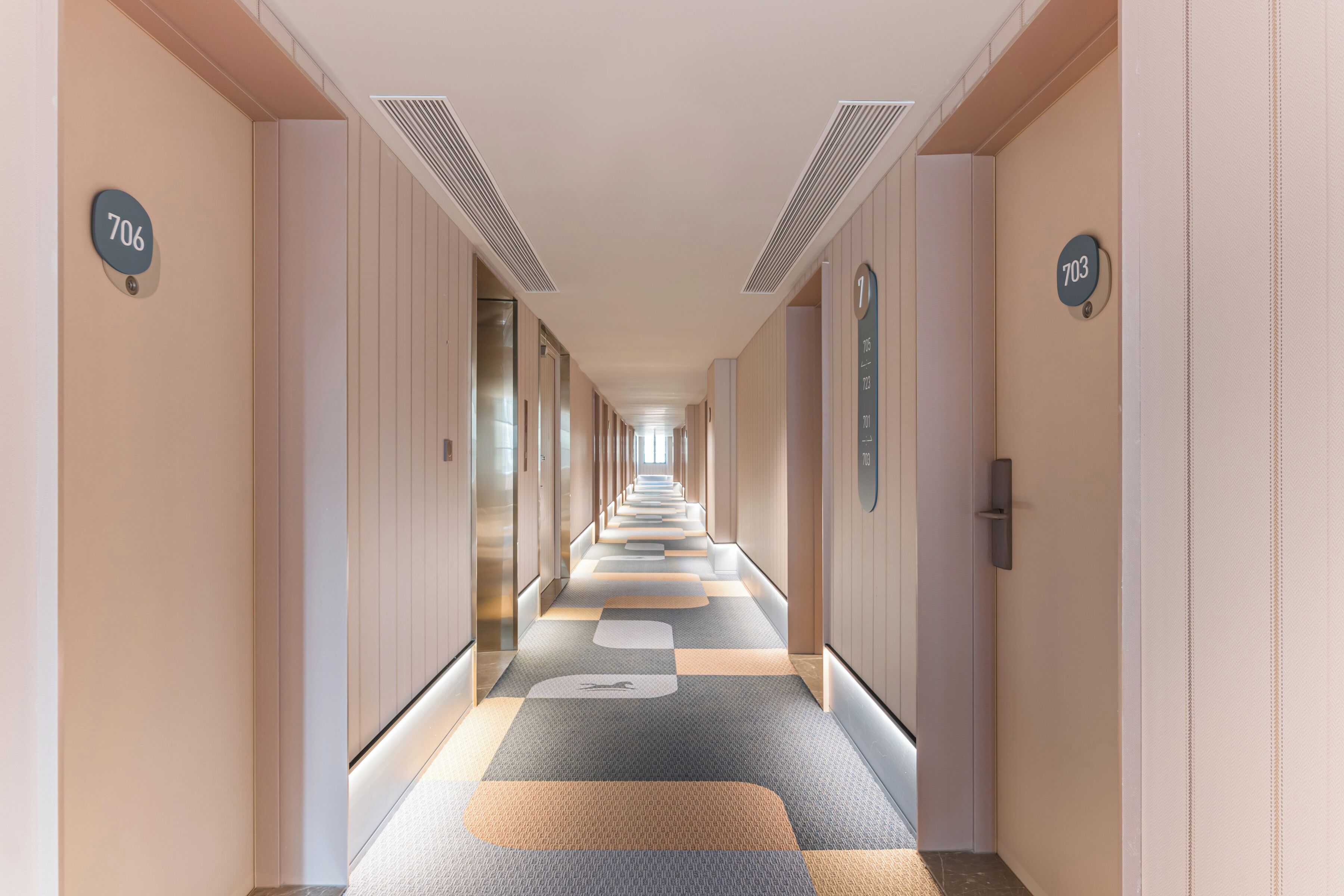 Un couloir d’hôtel avec des portes numérotées, une moquette à motifs et un design moderne.