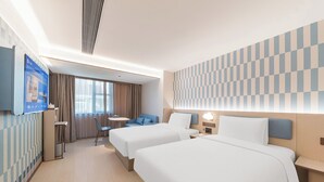 A hotel room with two beds, a desk, a TV, and a view of the city.
