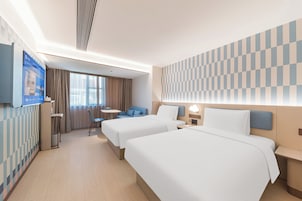 Habitación de hotel con dos camas, un escritorio, un televisor y vista a la ciudad.