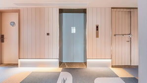 A hotel lobby with a central elevator, a reception desk, and a door with a number plate.