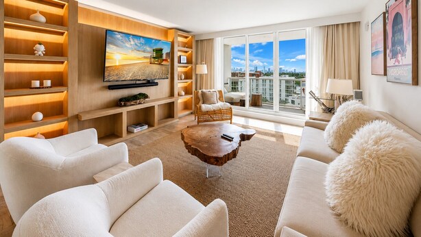 A modern living room with a large TV, comfortable seating, a wooden bookshelf, and a city view. - 1-bedroom hotel suites in amazing Miami Beach with fitness room (Miami Beach)