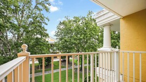 Un balcon donnant sur une pelouse et des arbres bien entretenus, avec une balustrade blanche et un mur jaune.