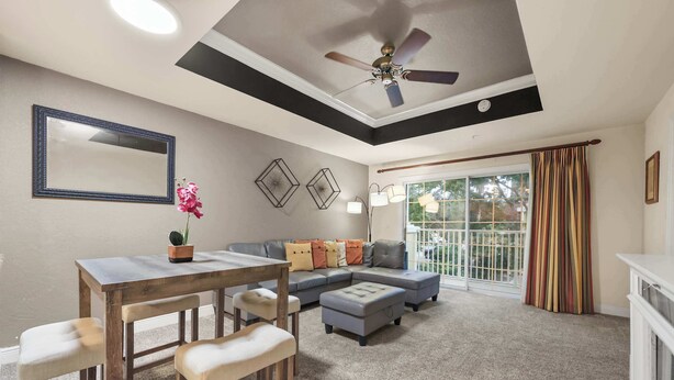 Un salon avec un ventilateur de plafond, une table à manger avec des chaises, un canapé et une grande fenêtre avec des rideaux.