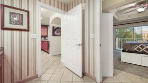 Un couloir aux murs rayés, une porte blanche et une chambre avec un lit et un balcon.