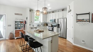 A modern kitchen with white cabinets, stainless steel appliances, and a central island with bar stools. - Low country luxury near Palmetto Bluff (Bluffton)