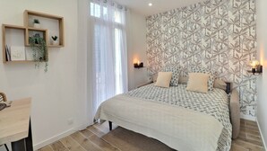 Quarto com cama, abajures, prateleira na parede com plantas e janela com cortinas.