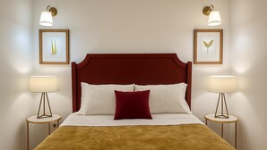 Un letto con testiera in legno, cuscini bianchi e rossi e copripiumino marrone con trama. Ci sono due comodini con lampade e opere d'arte incorniciate appese al muro.