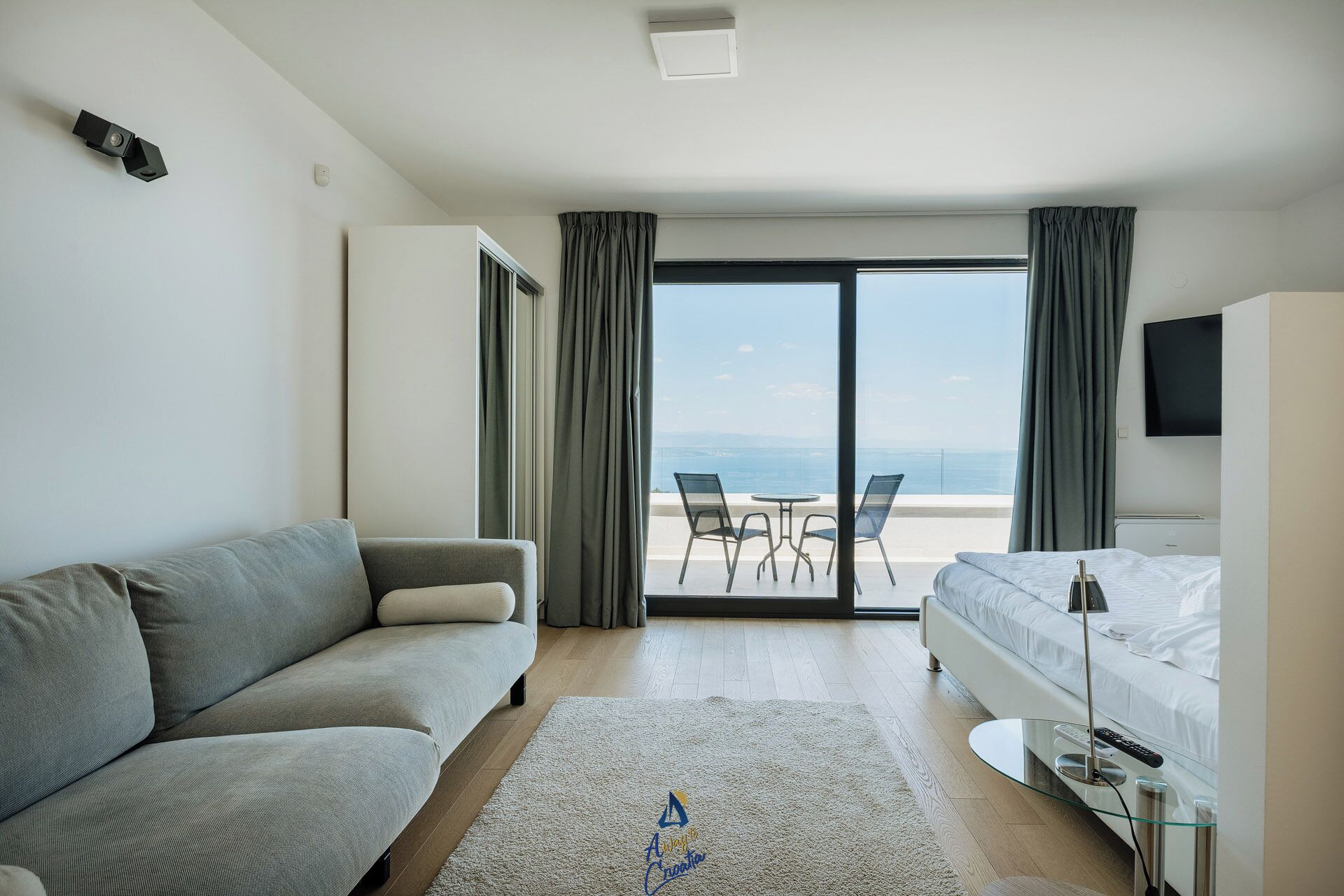 Habitación de hotel con sofá, cama, mesa de vidrio y vista al mar.