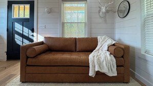 Un canapé en cuir marron dans une pièce aux murs en bois, avec une porte noire et une décoration représentant une tête de cerf.
