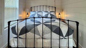 Une chambre à coucher avec un lit, un plafond en bois, des murs blancs et un appareil de climatisation.