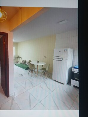 A kitchen with a white refrigerator, a dining table with chairs, and a green rug on the floor.
