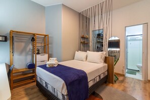 A bedroom with a bed, a wooden wardrobe, a mirror, and a bathroom with a glass door. - Studio 401 | 10 min from Lapa Arches | IV401 (Rio de Janeiro)