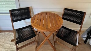Ein runder Holztisch mit zwei Stühlen, beide mit gewobener Sitzfläche und Lehne, in einem Raum mit Holzboden und schlichter Wand.