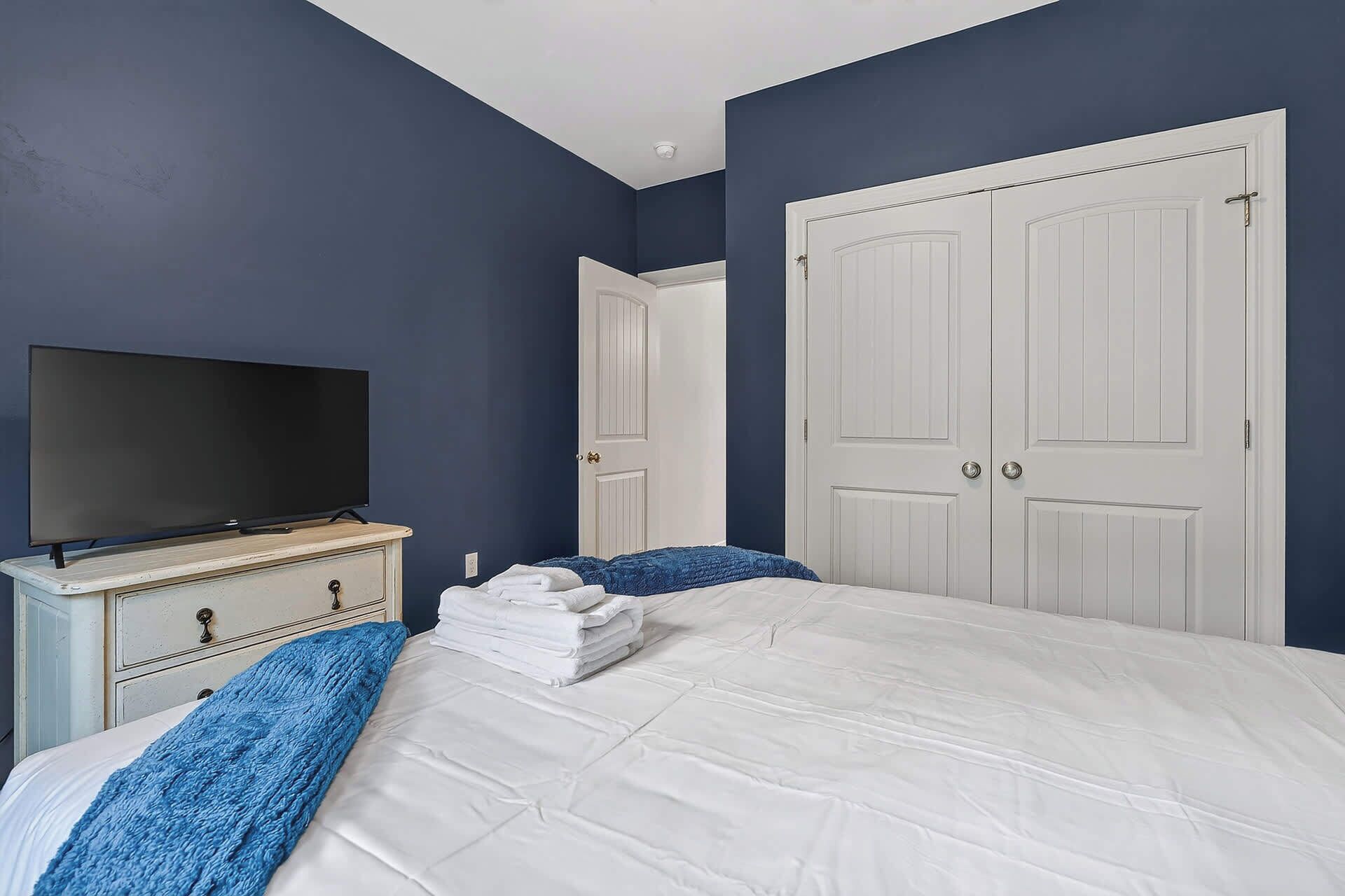 A bedroom with a bed, a TV on a dresser, and two doors.