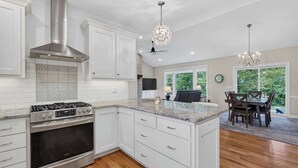 Una cocina moderna con armarios blancos, estufa de acero inoxidable y una isla grande con encimera de mármol.