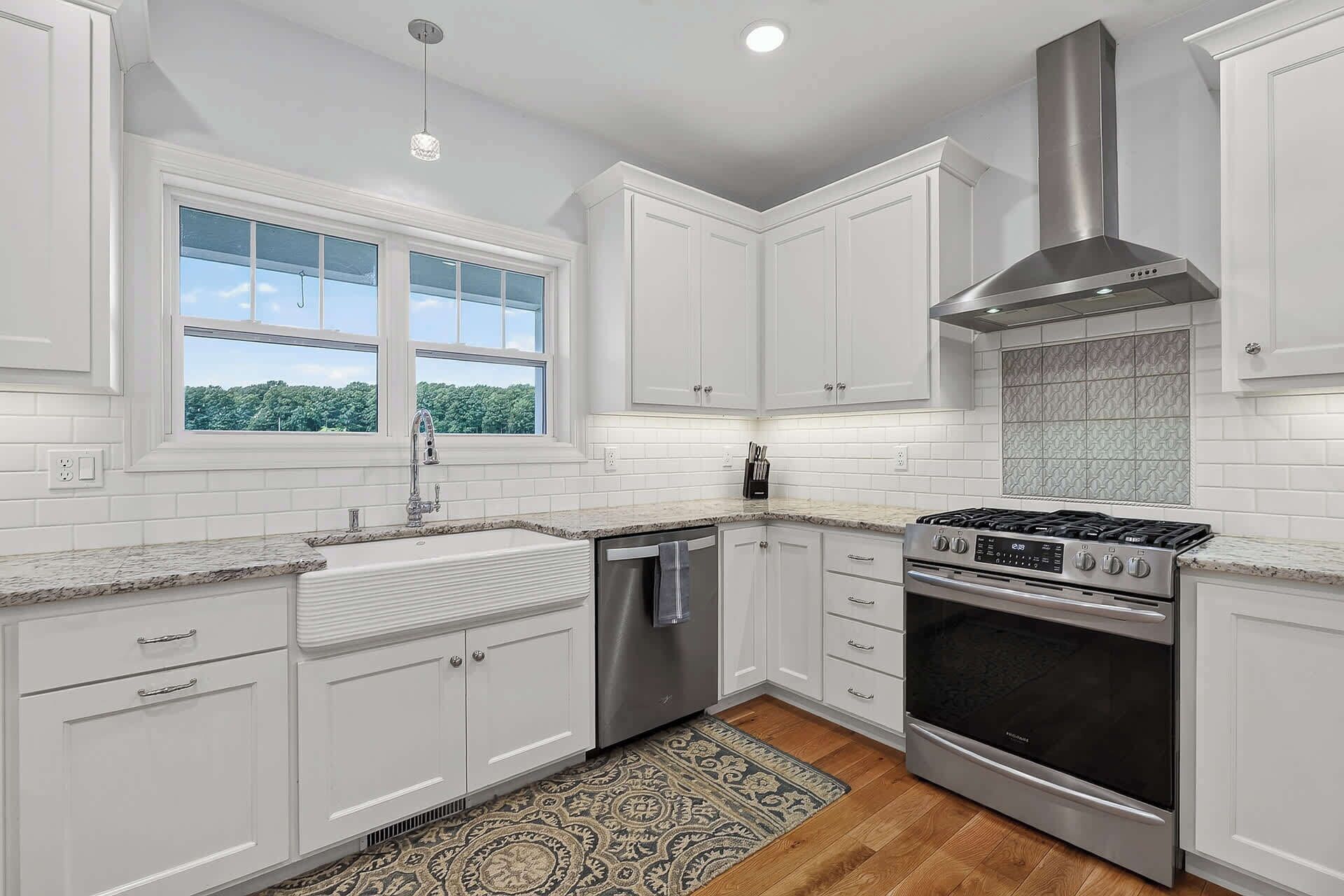 A kitchen with white cabinets, a stainless steel range, a dishwasher, and a window with a view of greenery.