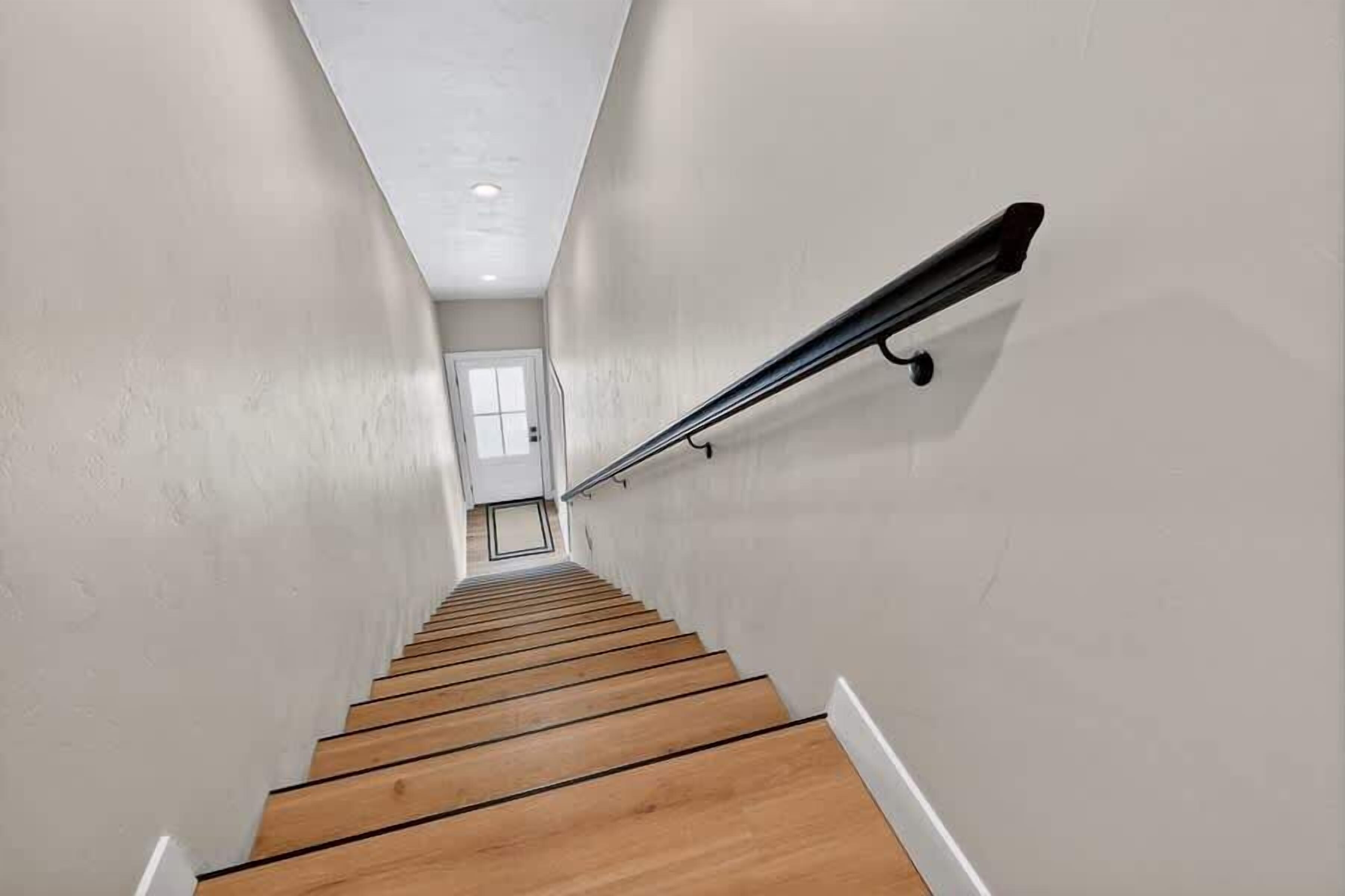 Un escalier avec des marches en bois et une rampe noire, menant à une porte située en haut.