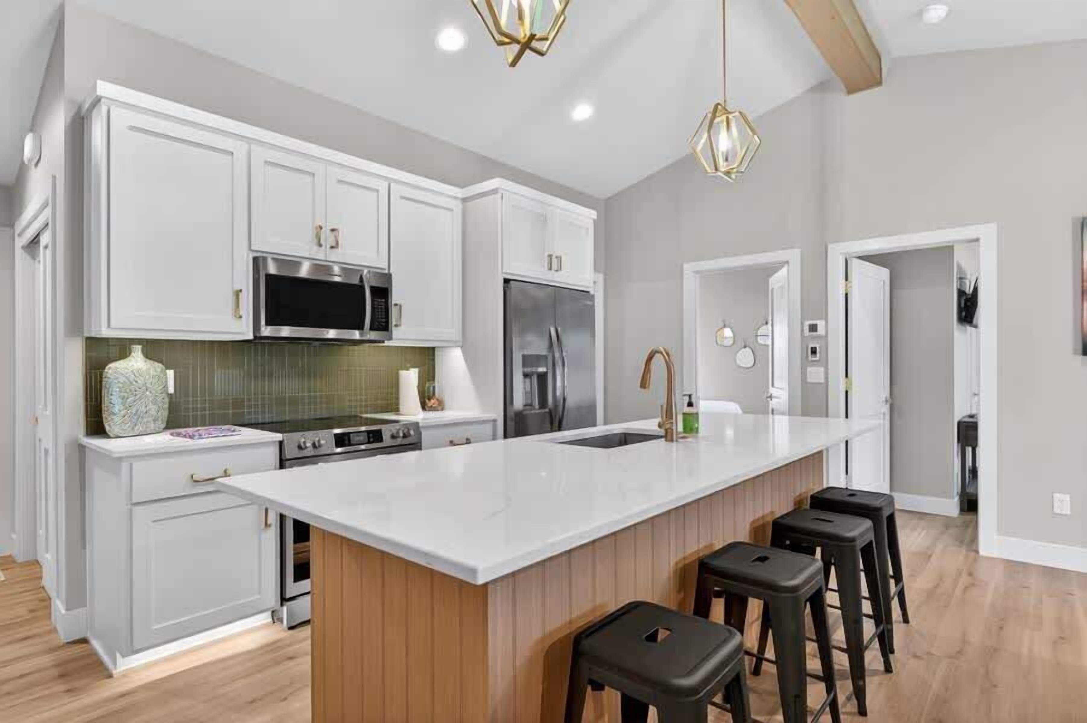 A modern kitchen with white cabinetry, a large island with stools, stainless steel appliances, and a pendant light.