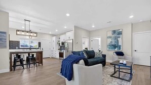 A modern living room with a sofa, coffee table, and bar stools. There is a kitchen area with cabinets and appliances in the background. - Sturgeon Bay Boat Condo w Marina Slip (Sturgeon Bay)