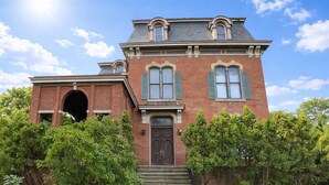A two-story brick building with a central entrance, a staircase leading up to it, and a large arched window on the left.
