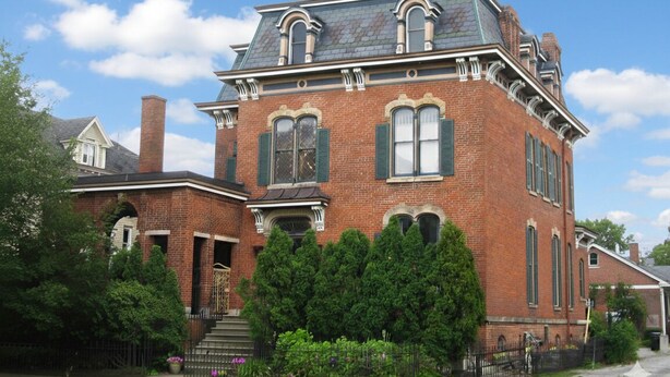 A large, historic brick building with a prominent gabled roof, large windows, and a front entrance with steps.
