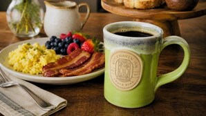 A breakfast setting with scrambled eggs, bacon, berries, toast, and a mug on a wooden table.