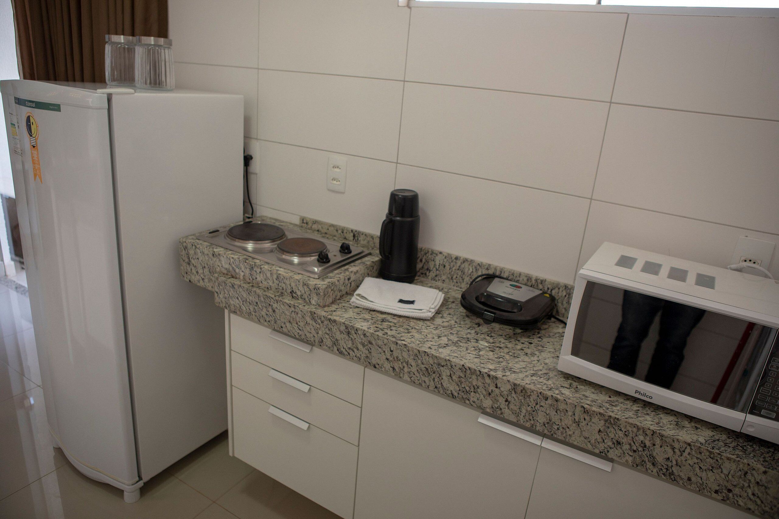 Uma cozinha com geladeira branca, bancada de granito, micro-ondas e cafeteira.
