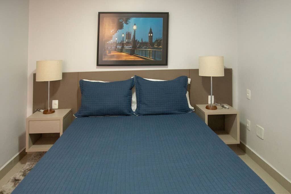 A hotel room with a large bed, two bedside tables, lamps, and a framed picture of a cityscape.