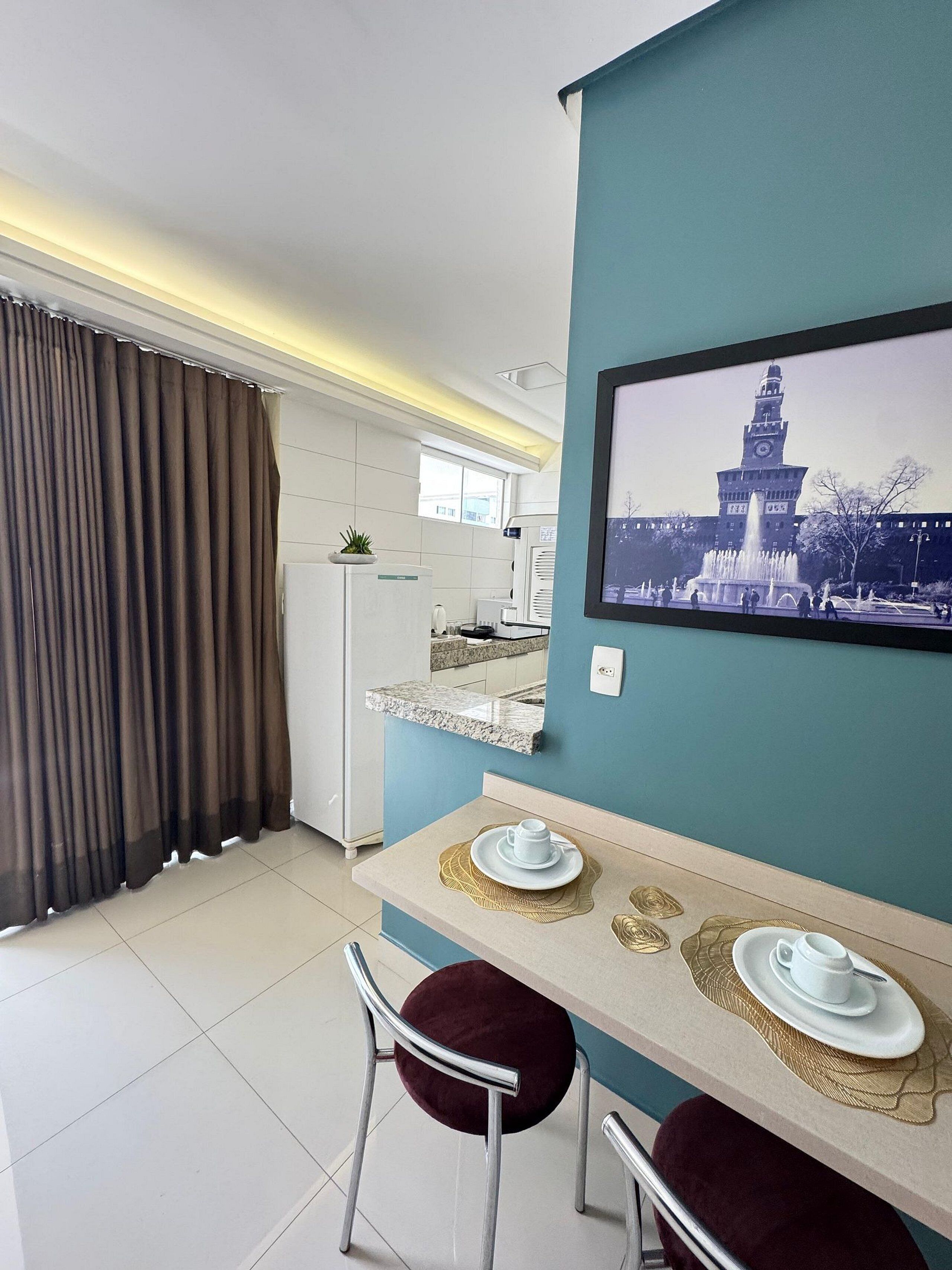 Cocina moderna con refrigerador, pileta y ventana. Cuenta con comedor, mesa, sillas y un cuadro en la pared.