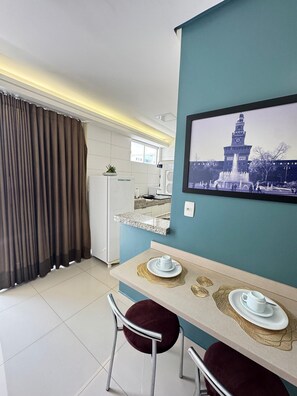 A modern kitchen with a refrigerator, a sink, and a window. There is a dining area with a table, chairs, and a framed picture on the wall. - Ônix Bueno Residence (Goiânia)