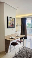 Uma área de refeições moderna com uma mesa de madeira, duas cadeiras, uma luminária pendente e uma obra de arte emoldurada na parede.