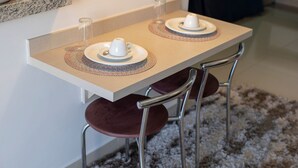A small table with two white cups on saucers, a spoon, and a woven placemat.