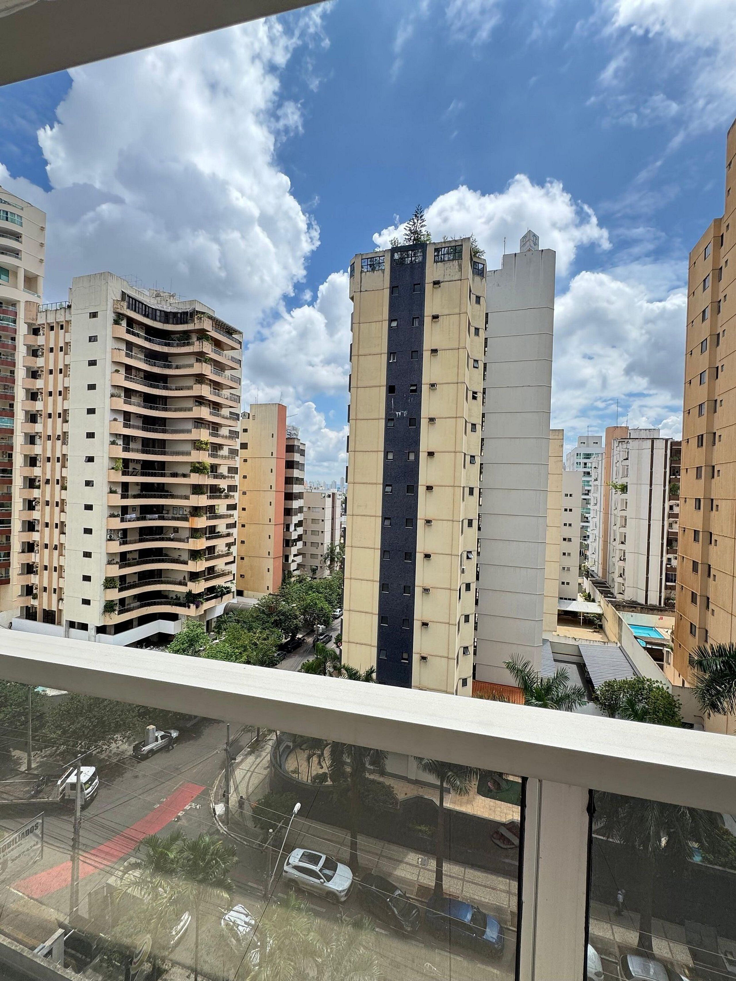 Edifício residencial alto com várias varandas, céu claro e estruturas urbanas ao redor.