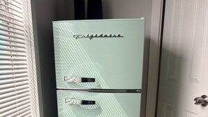A light green refrigerator with the brand name 'Ergidaire' in the corner, located in a corner of a room with a tiled floor and a door in the background.