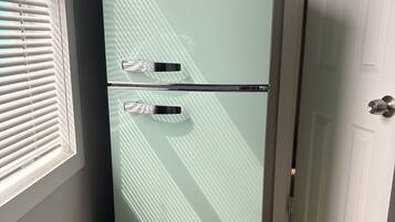 A light green refrigerator with the brand name 'Ergidaire' in the corner, located in a corner of a room with a tiled floor and a door in the background.