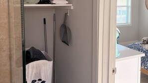 A bathroom with a shower, a towel rack, a cleaning mop, and a pet bed.
