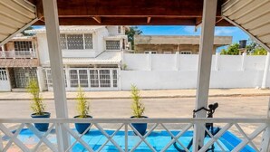 A covered balcony with a view of a swimming pool, white railings, and potted plants. - La Casa del Ancla - A beautiful nautical cabin! (San andrés)