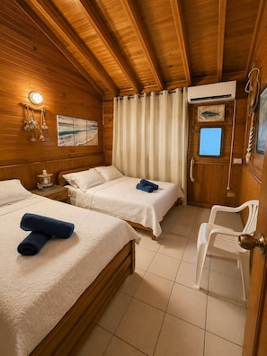 A cabin with two beds, a small table, a chair, a window, and a wall-mounted air conditioner. - La Casa del Ancla - A beautiful nautical cabin! (San andrés)
