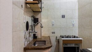Cocina compacta con lavamanos, estufa y estanterías.